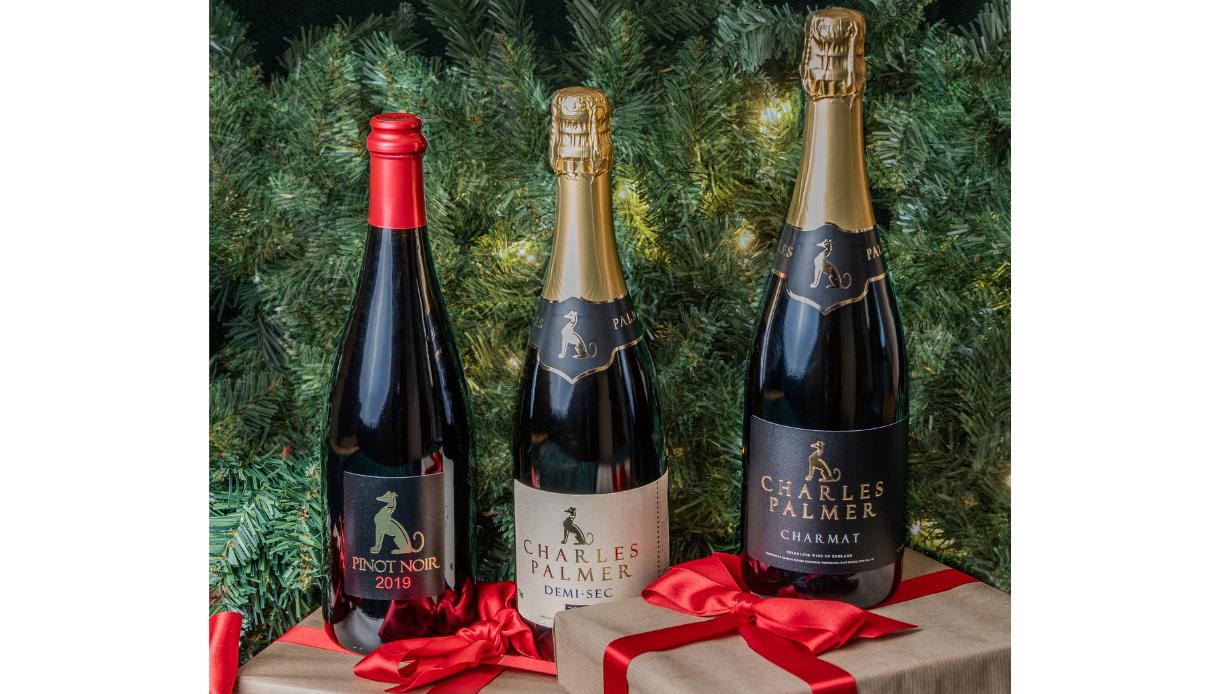 Three Charles Palmer wine bottles with festive ribbons in front of a green Christmas tree background.
