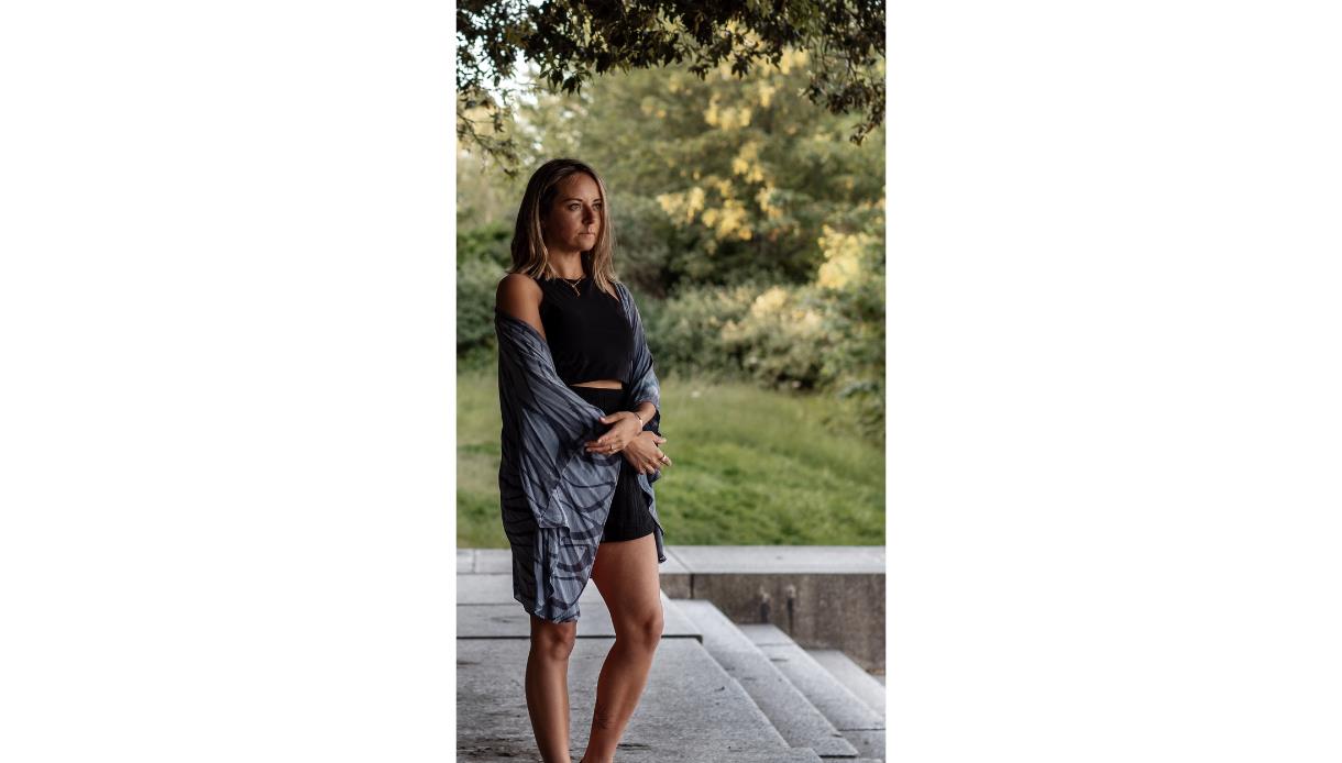 Image shows a person stanading outside looking into the distance. They are dressed casually for yoga and look like they are reflecting.