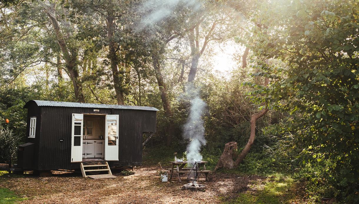 Shepherd’s hut by The Original Hut Company near Bodiam, with a smoking fire pit and wooden seating in a woodland clearing.