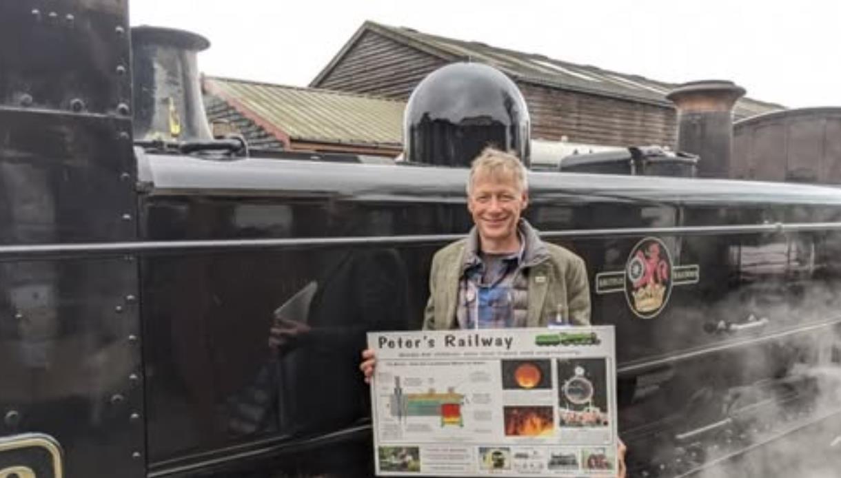 Person holding a poster in front of a steam locomotive at the Kent and East Sussex Railway.