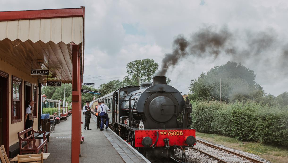 Kent and East Sussex Heritage Railway with a black steam locomotive at a station platform, emitting smoke.