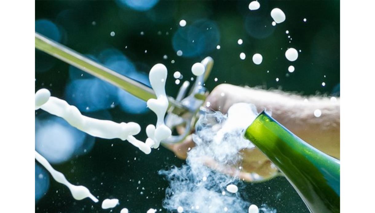 A sword slices open a champagne bottle, sending spray and foam bursting into the air.