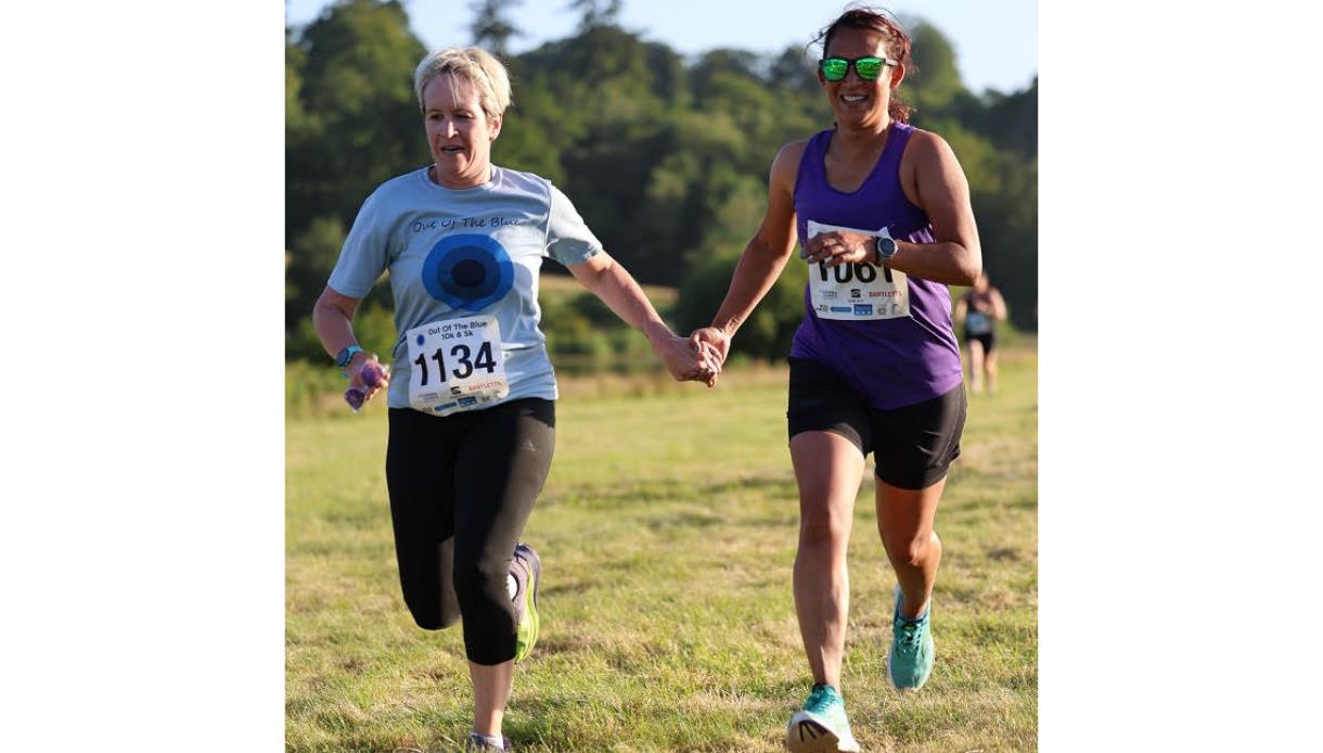 Two runners holding hands as they race across a grassy field on a sunny day.