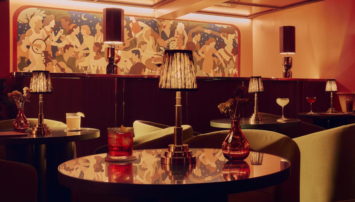 Elegant bar at Powdermills Hotel with round tables, cocktails, warm lighting, and a colourful mural backdrop.