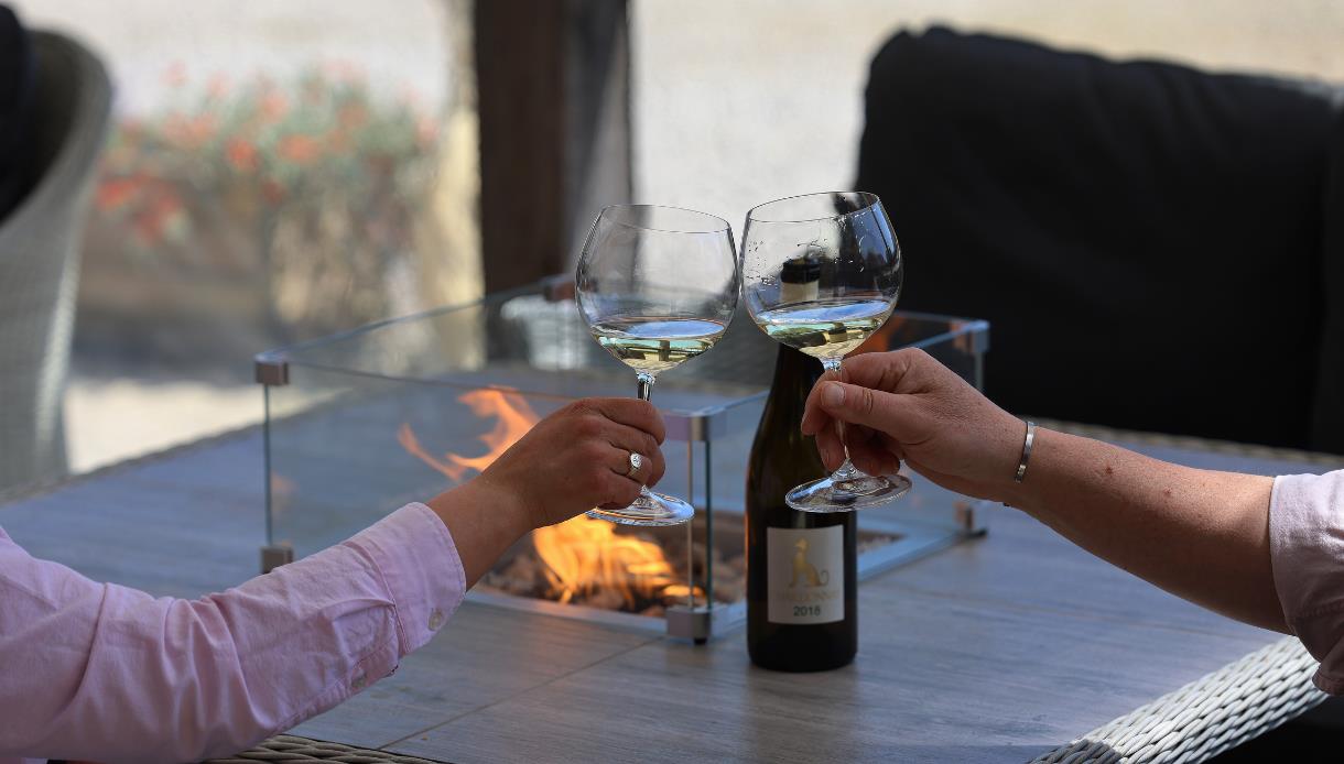 Two people raising glasses of white wine beside a tabletop fire at Charles Palmer Vineyards.