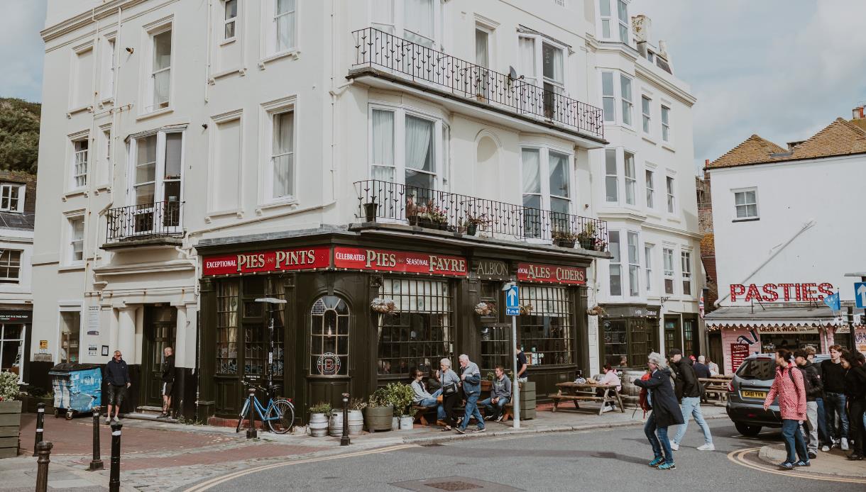 Exterior of The Albion pub on a Hastings street corner, with people sitting outside and nearby shops.