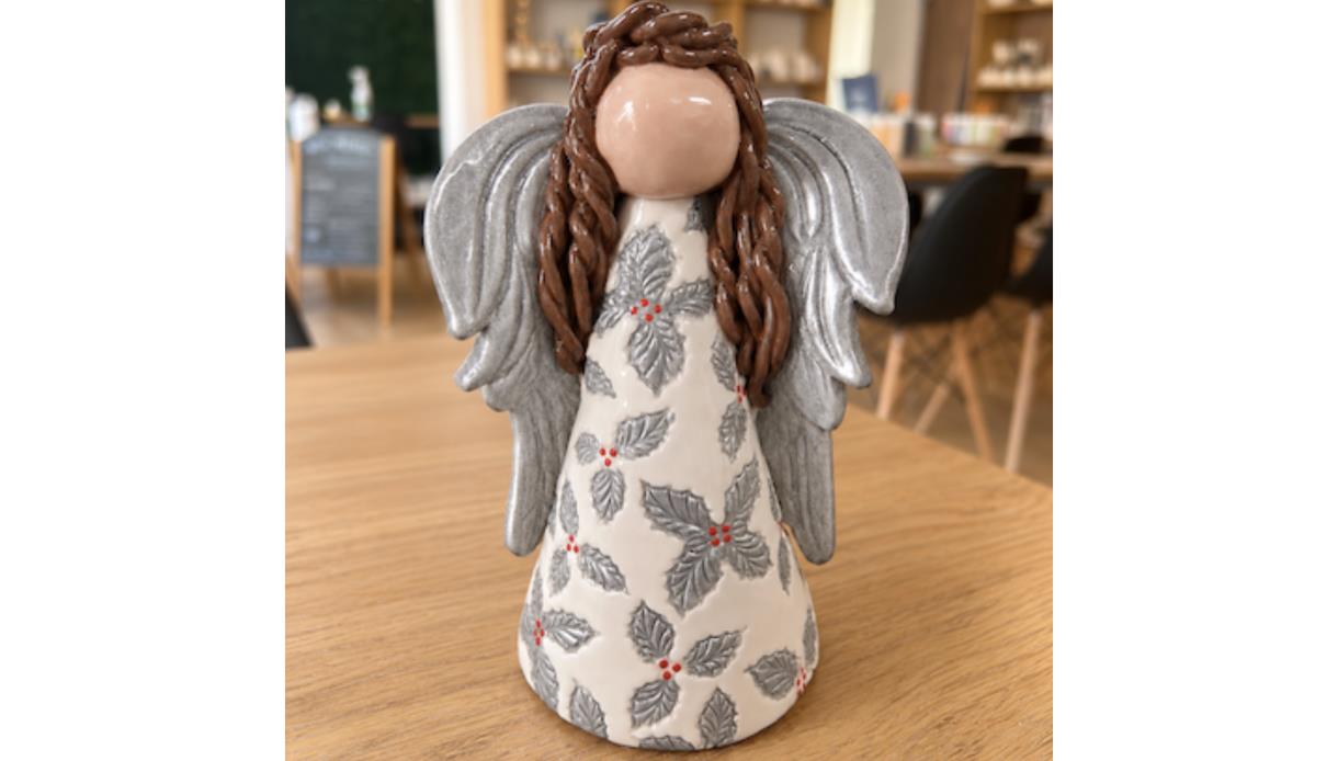 Handcrafted ceramic angel with silver wings and holly-patterned robe displayed during a Christmas pottery workshop