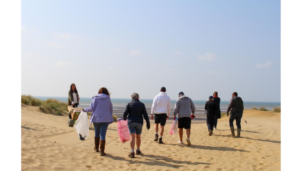 Community beach clean at the Gallivant, Camber, with volunteers walking across sand dunes carrying litter bags.