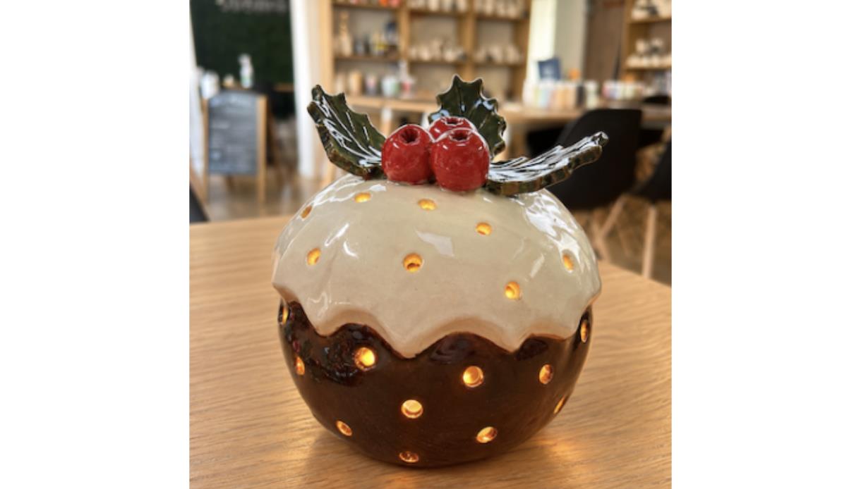 Handcrafted ceramic Christmas pudding lantern with holly decoration and glowing cut-out details from a pottery workshop