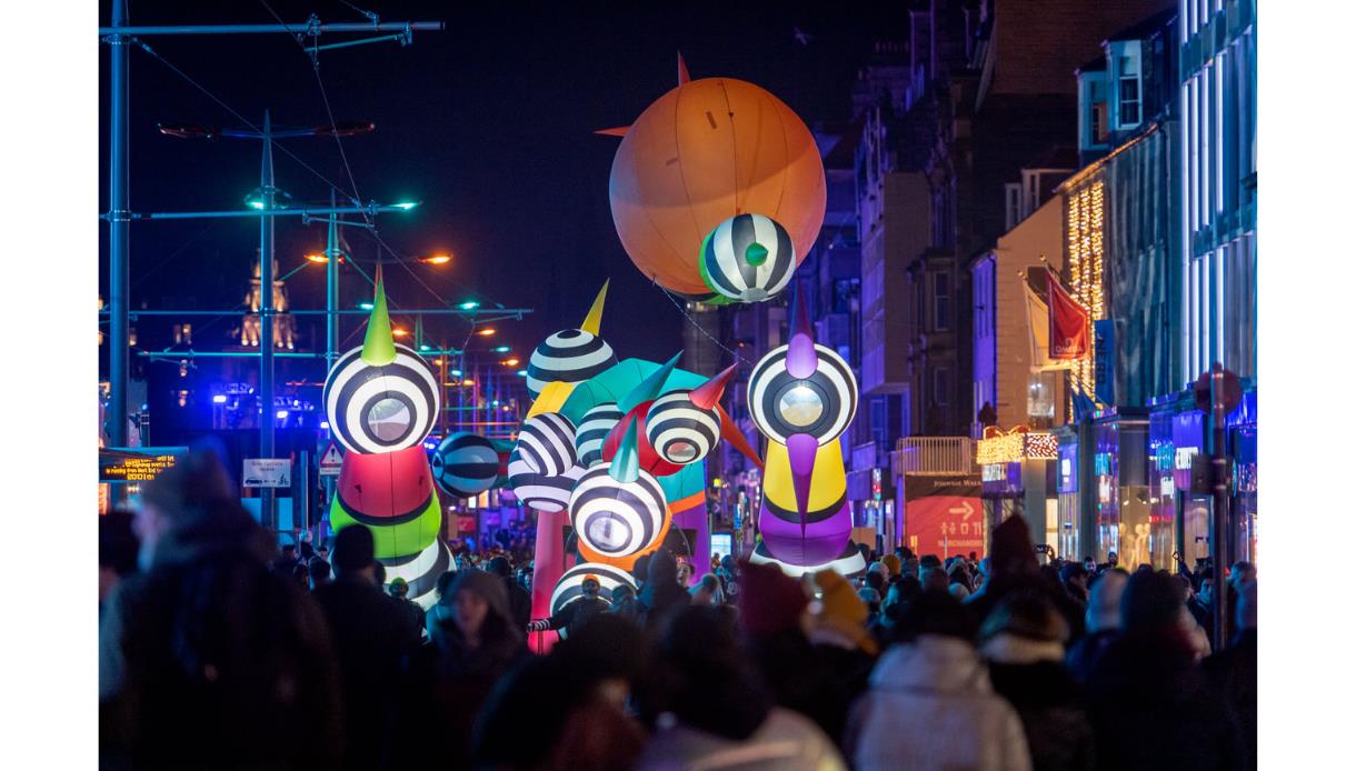Crowds enjoy an 18 Hours event with large illuminated sculptures lighting up a city street at night.