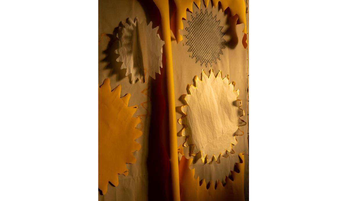 Abstract paper installation with layered cream, yellow and patterned cut-out shapes, lit by warm golden light.
