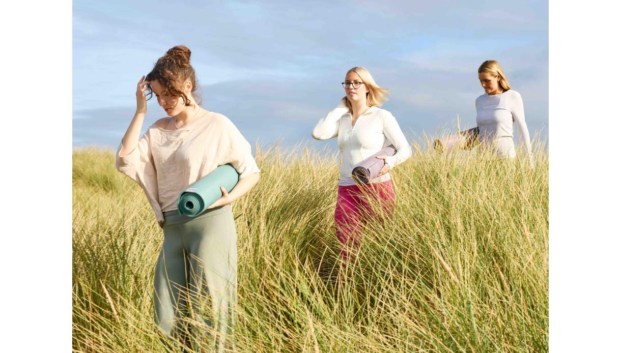 Participants carrying yoga mats walk through grassy dunes at The Gallivant for Strawberry Moonrise Yoga.