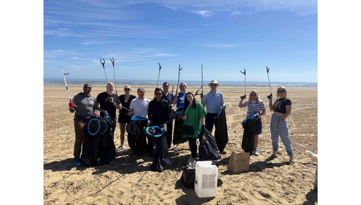Community volunteers on a sandy beach holding litter pickers and rubbish bags during a community beach clean event.