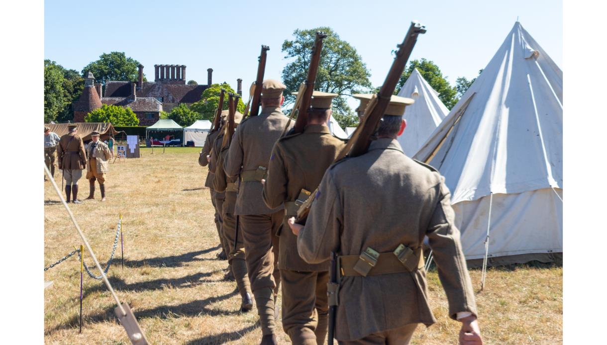 WW1 reenactors marching with rifles past canvas tents on a grassy field during a historical weekend at Bateman’s.