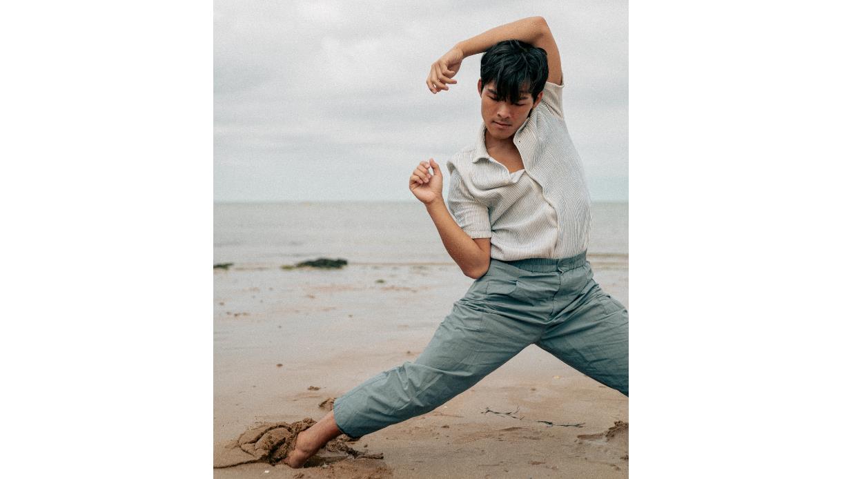 Yoga artist David Kam performs a fluid, expressive pose on a beach, arms raised and legs grounded in sand, from Beyond Asana.