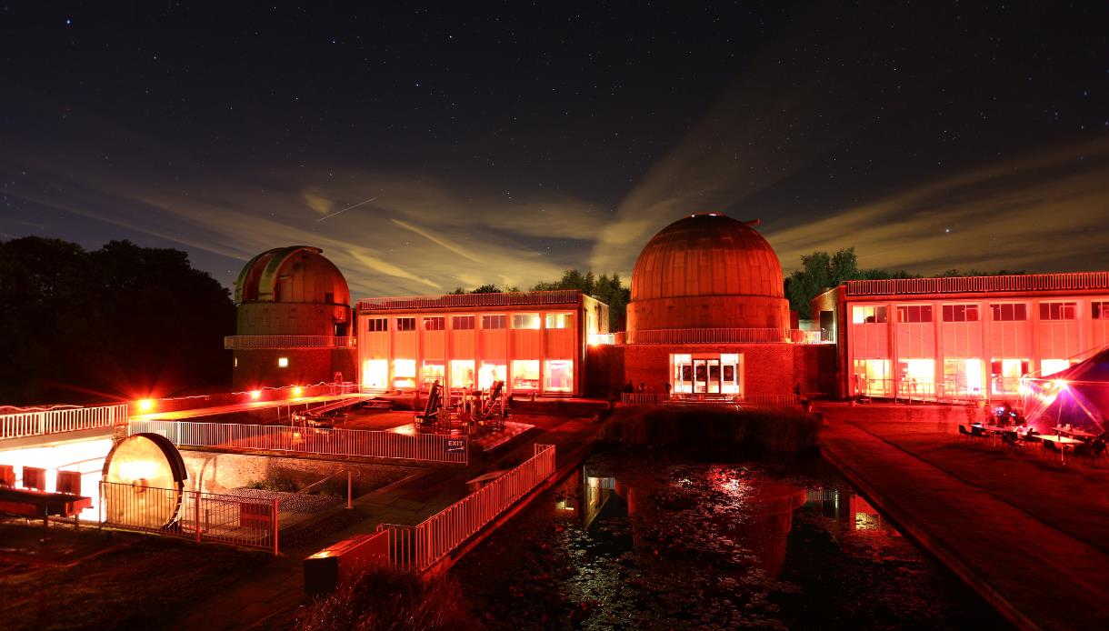 The Observatory Science Centre at night, illuminated in red with telescope domes under a starry sky.