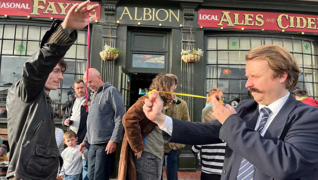 People compete in a traditional conkers match outside The Albion pub, watched by a crowd of spectators.