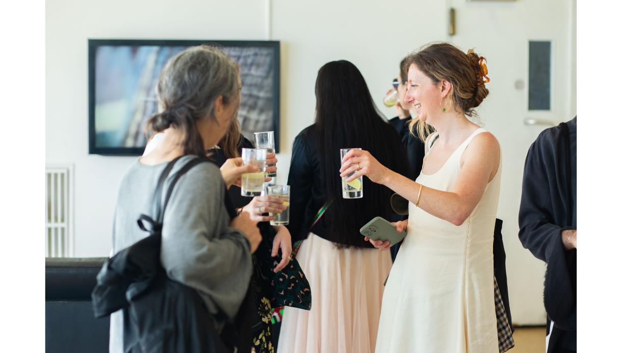 Guests with drinks chat at summer exhibition opening, De La Warr Pavilion, Bexhill, artwork in background.