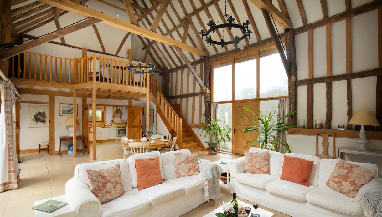 Spacious barn-style interior with exposed beams, mezzanine, wooden staircase and cosy seating area.