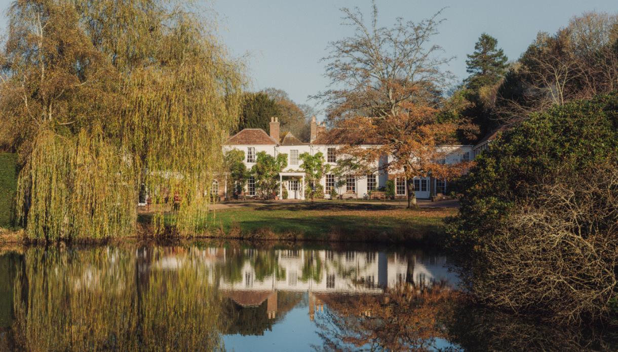 Crafted at Powdermills Hotel reflected in a lake, surrounded by autumn trees, showcasing serene countryside setting.