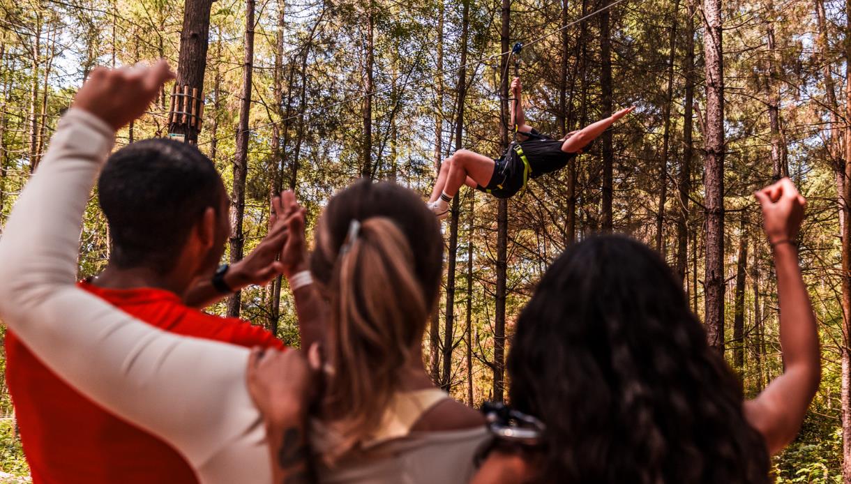 Adults-only group cheering as a participant rides a zip line through the forest at Go Ape treetop adventure.