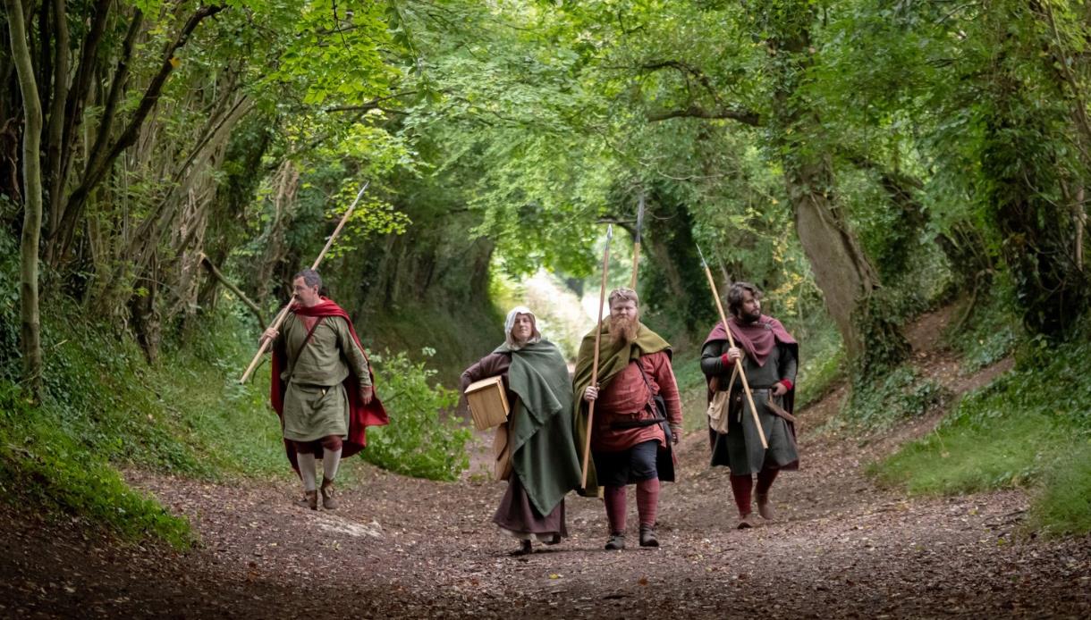 Historical reenactors walking along a woodland path with spears and cloaks, promoting Meet the Haestingas at Hastings Museum & Art Gallery