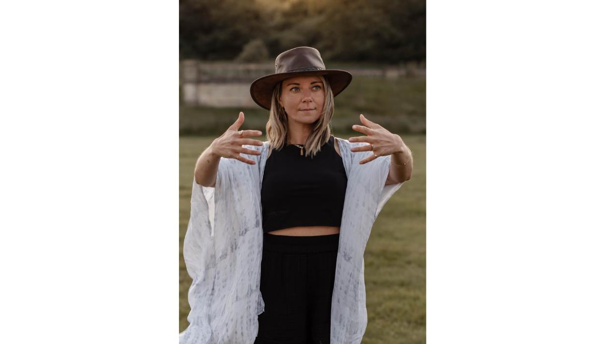 Facilitator stands outdoors with arms open in a guided movement pose, promoting Summer Transformational Breathwork at The Gallivant.