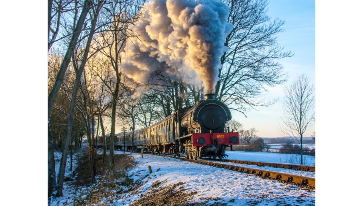 Steam locomotive travelling through a snowy countryside, billowing steam, during the Steam Into New Year railway event.