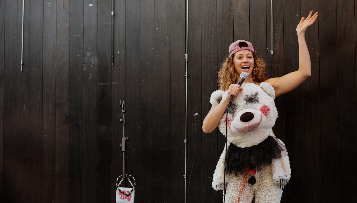 Performer in a bear-themed costume holding a microphone onstage during ‘New Work Night – Titus Andronicus.’