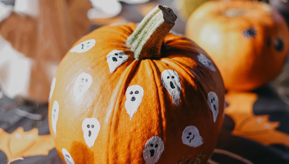 Close-up of a pumpkin decorated with painted ghost faces, promoting an autumn storytelling and woodland event