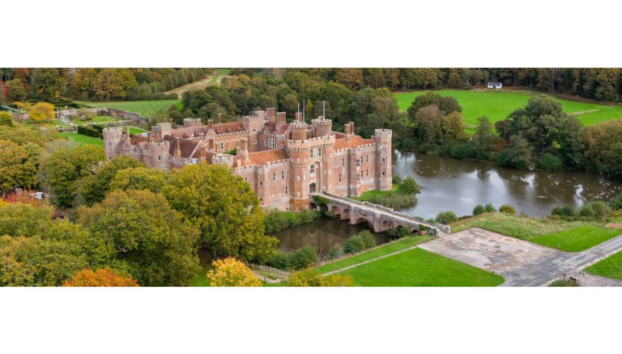 Aerial view of Herstmonceux Castle surrounded by autumn trees and lawns.