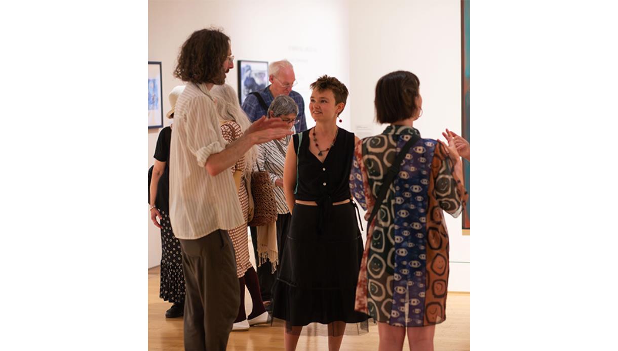 Visitors in conversation during a gallery event at De La Warr Pavilion, surrounded by exhibition artworks.