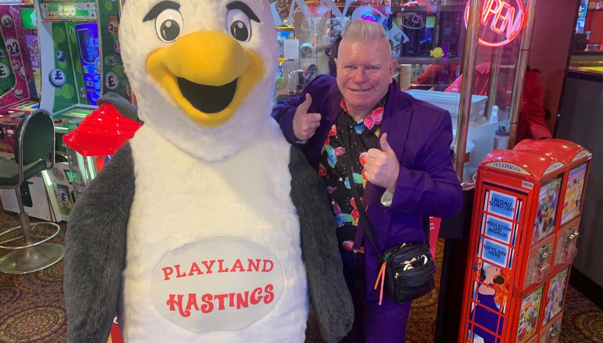 Playland Hastings mascot penguin with entertainer inside colourful amusement arcade, surrounded by games and prizes.