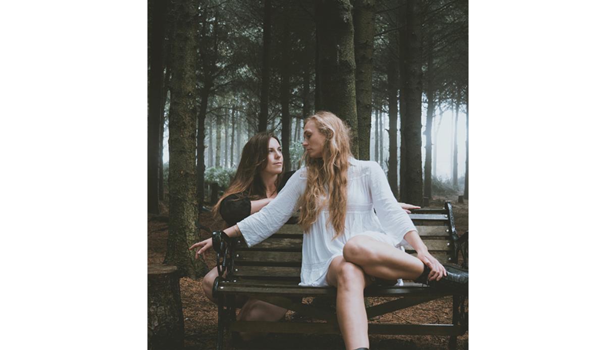 Promotional image for True Foxes at De La Warr Pavilion, showing two performers seated on a bench in a wooded setting.