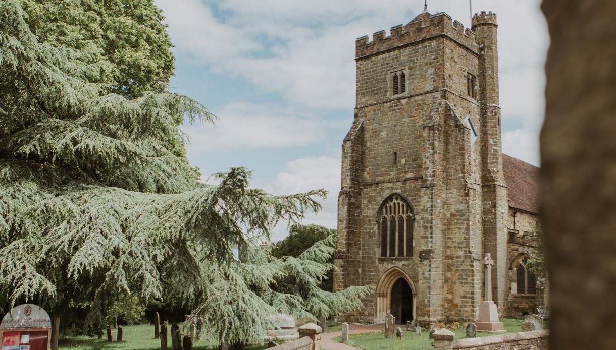 St Mary's Church in Battle, framed by mature trees and historic gravestones on a bright day.