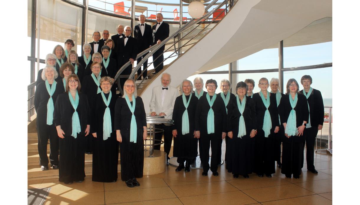 Bexhill Choral Society posed on a staircase at De La Warr Pavilion in concert dress, promoting a performance of Mendelssohn’s Elijah.