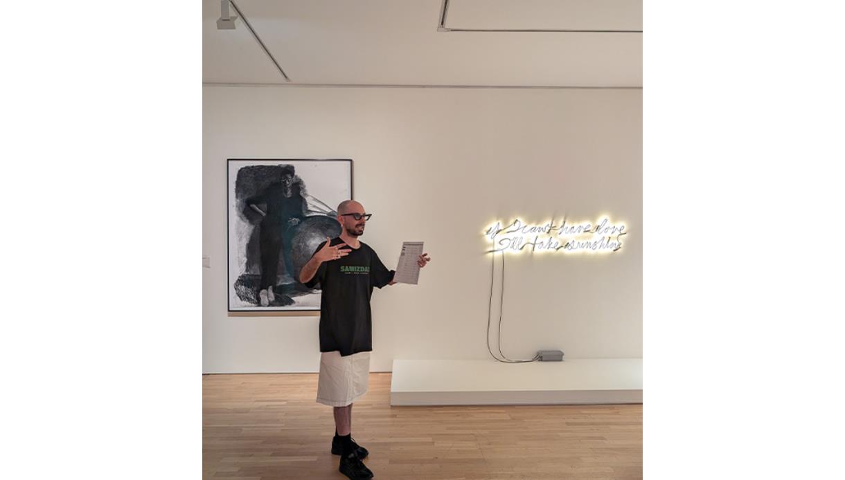 Person leading a gallery tour beside contemporary artworks and a neon installation at De La Warr Pavilion.