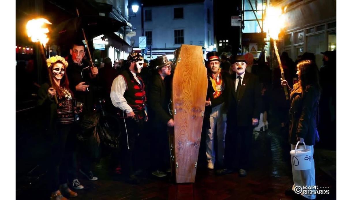 Torchlit Hastings Voodoo Fest parade with costumed participants, painted faces and a coffin carried through night streets.