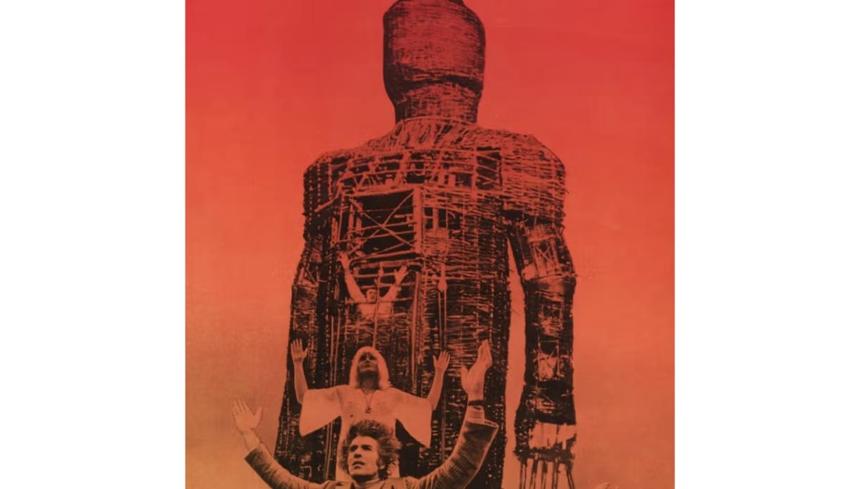 Promotional image for The Wicker Man showing a giant wicker figure towering above raised figures against a red sky.