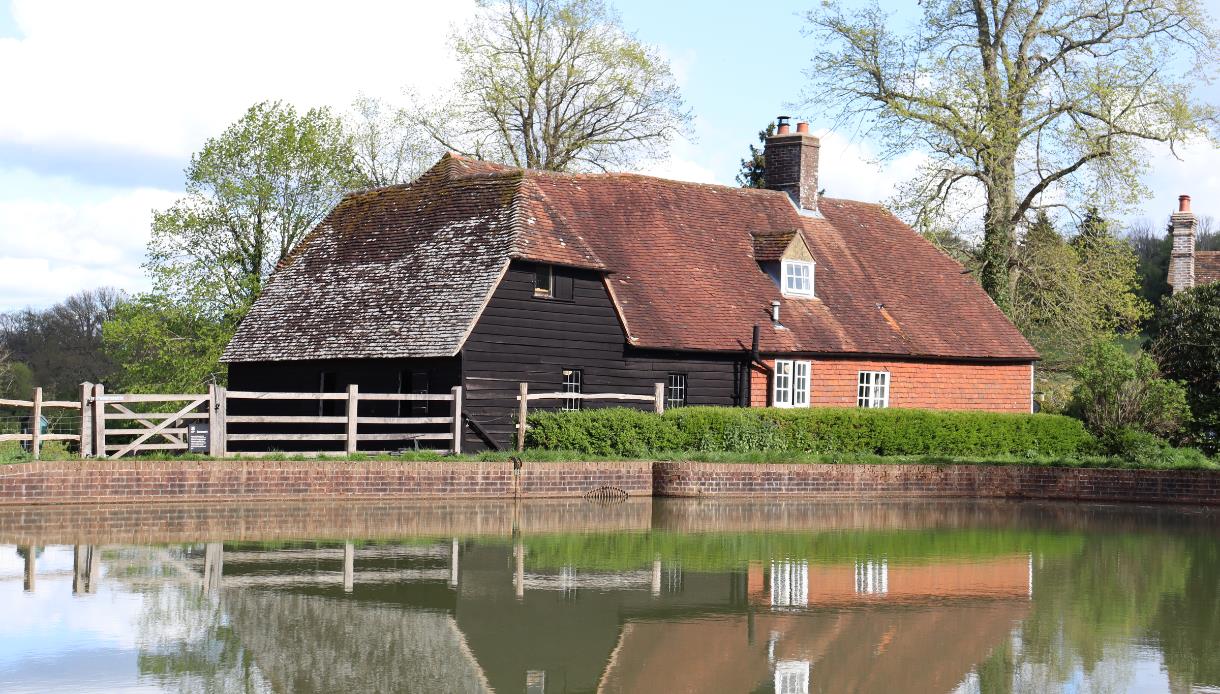Park Mill at Bateman’s during Mill Weekend, with a historic red‑tiled mill building reflected in the surrounding water.
