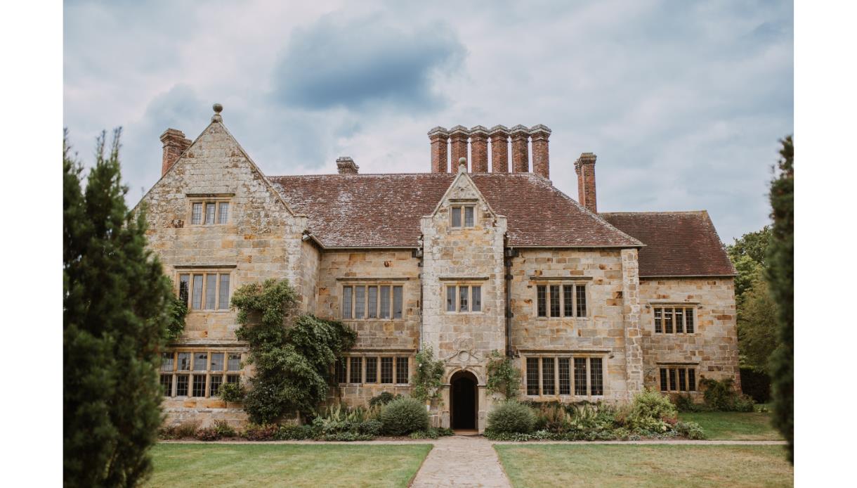 Batemans, a historic stone manor with tall chimneys and gardens, seen from the front on a cloudy day.
