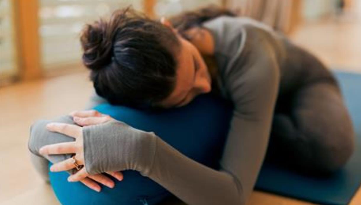 Person resting on a blue bolster while lying on a yoga mat in a relaxed pose indoors.