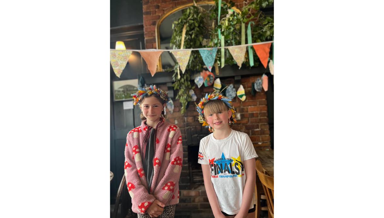 Two children wearing handmade flower crowns at a workshop in The Crown pub in Hastings, with bunting and decorations.