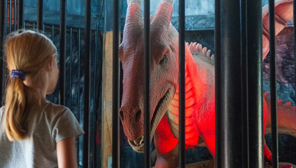A child looks at a large red dragon figure behind bars, illuminated by red light at Knockhatch.