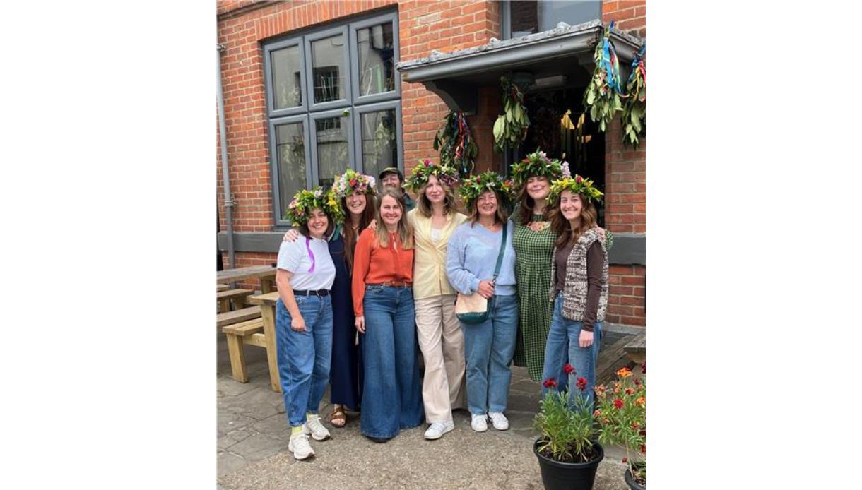 Group wearing colorful flower crowns outside The Crown in Hastings during a workshop, with plants and decorations nearby.
