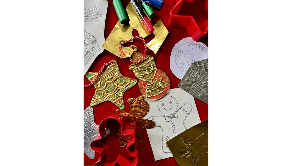 Overhead view of DIY holiday ornament making. Mixed materials include shiny gold and silver foil pieces with stamped patterns, finished ornaments (tre