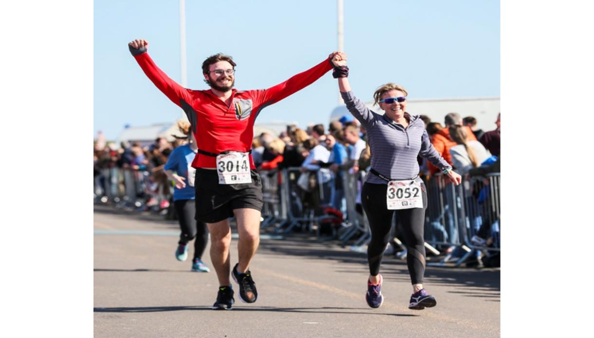 Focused runners mid-stride during an outdoor street race, urban backdrop with barriers and onlookers.