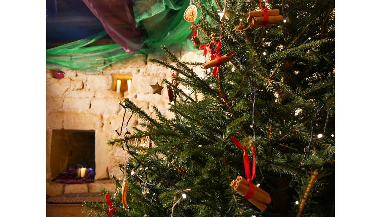 image shows a festive christmas tree inside Bodiam castle. On the tree are cinnamon sticks, lights and decorations