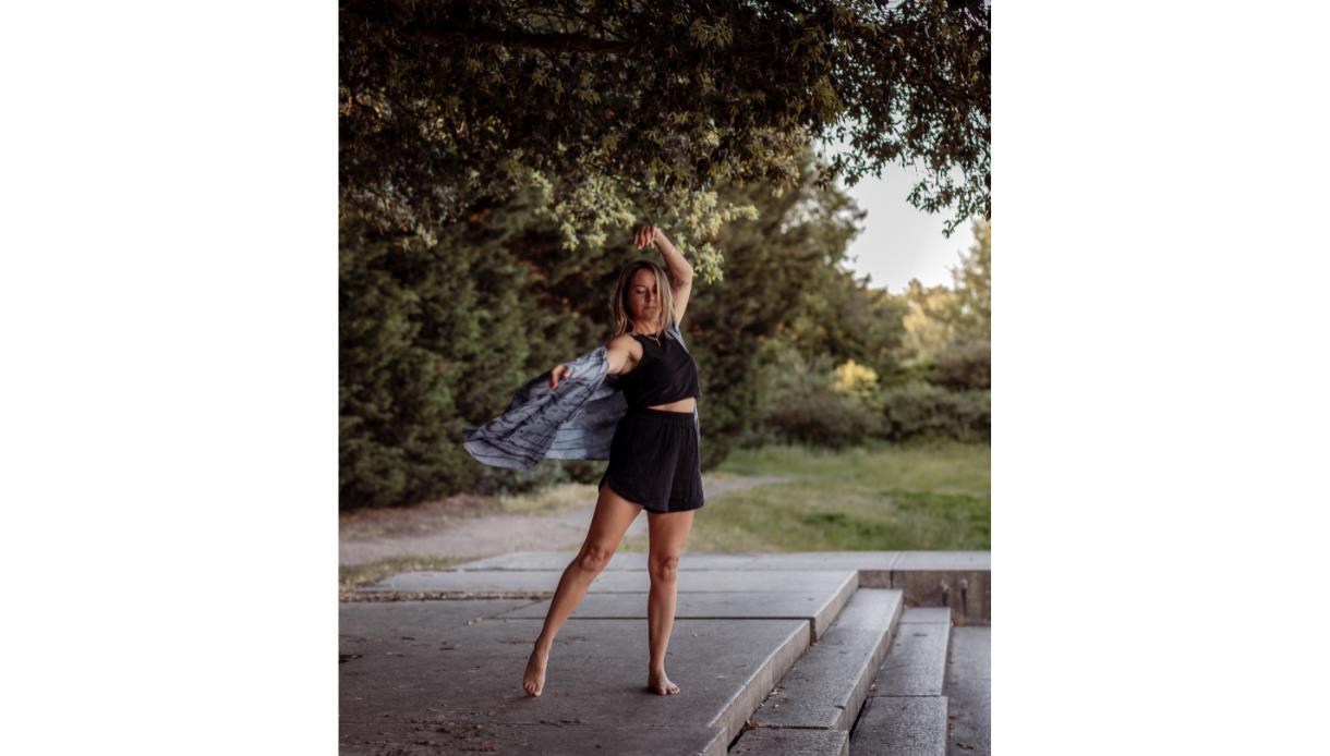 A woman is outdoors on a patio area moving her body. Her clothes flow in the movement.