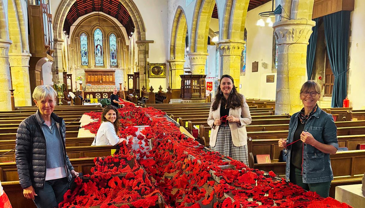 Image shows the inside of St Marys Church with the handmade poppys for the event. There are 4 members of the team standing with the poppys.